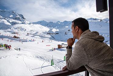 Homme sur le balcon de la résidence Le Cheval Blanc vue pistes à Val Thorens